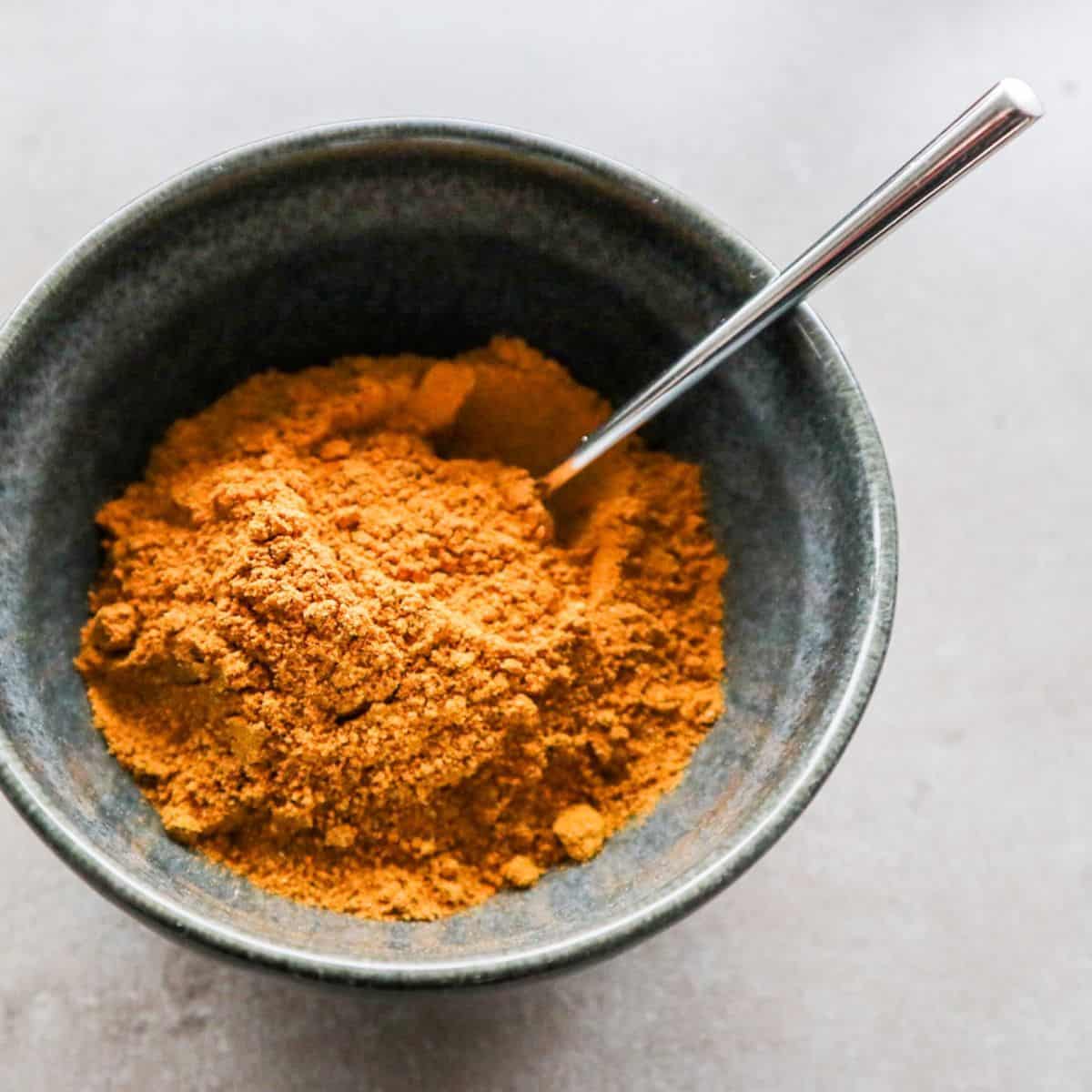 Homemade curry powder substitute in a grey bowl with a spoon.
