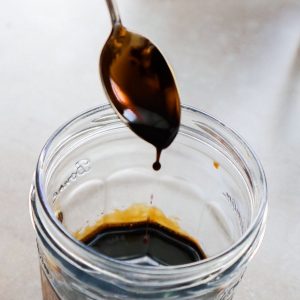 Balsamic reduction on a spoon with a grey background.
