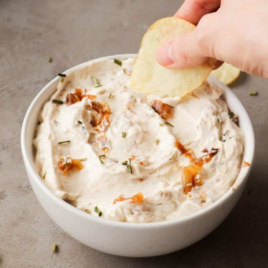 Caramelized onion dip with a hand and some crisps.