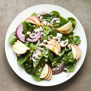 Spinach salad with feta cheese, Apple and honey mustard dressing on a white plate.