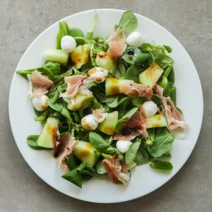 A melon and prociutto salad on a plate.