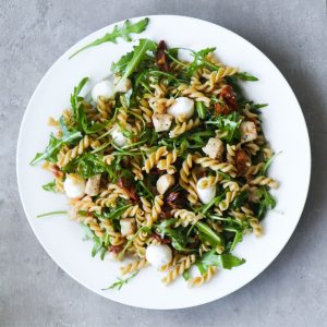 Summer pasta pesto salad with chicken and mozzarella on a white plate.