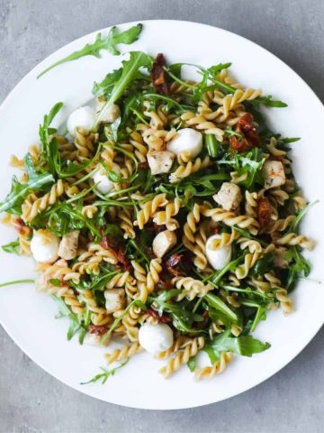 Summer pasta pesto salad with chicken and mozzarella on a white plate.