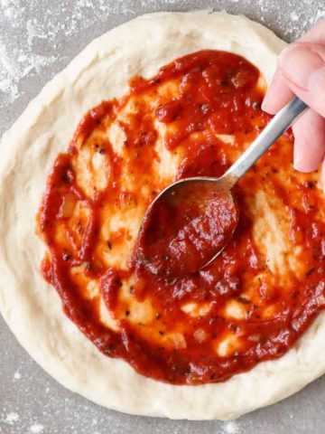 Pizza sauce spread on pizza dough with a spoon.