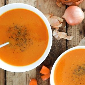 Carrot celery soup in white bowls on wood.
