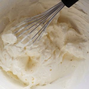 Whipped cream and a whisk in a white mixing bowl.