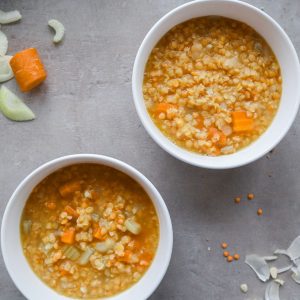 Two bowls of vegan lentil soup on a grey background.