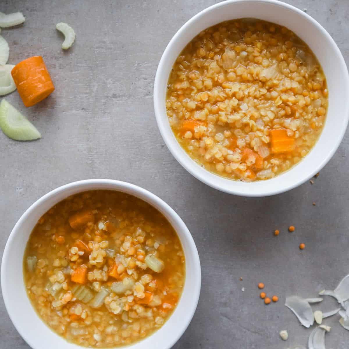 Two bowls of vegan lentil soup on a grey background.