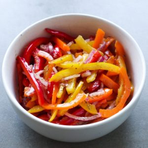 A side shot of a white bowl with bell pepper salad on a grey background.
