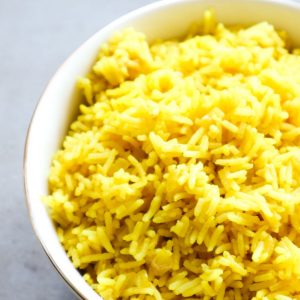 Yellow rice in a white bowl on a grey background with onions and turmaric.