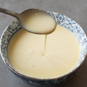 A close-up of a spoon dipped in vanilla sauce above a delft blue bowl.