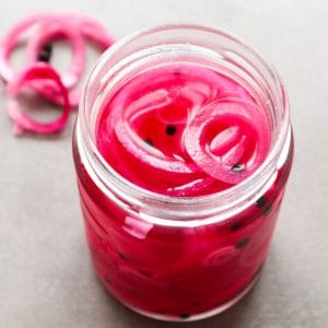 A close up of pink pickles onions with pepercorns.
