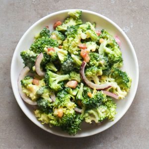 An overhead shot of a broccoli salad with onion and bacon on a white plate.