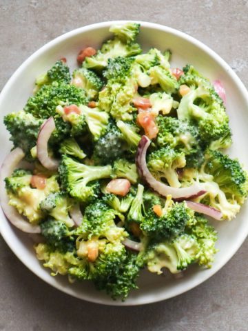 An overhead shot of a broccoli salad with onion and bacon on a white plate.