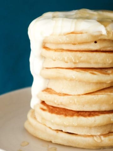 Pancakes made with oat milk on a white plate with a blue background.