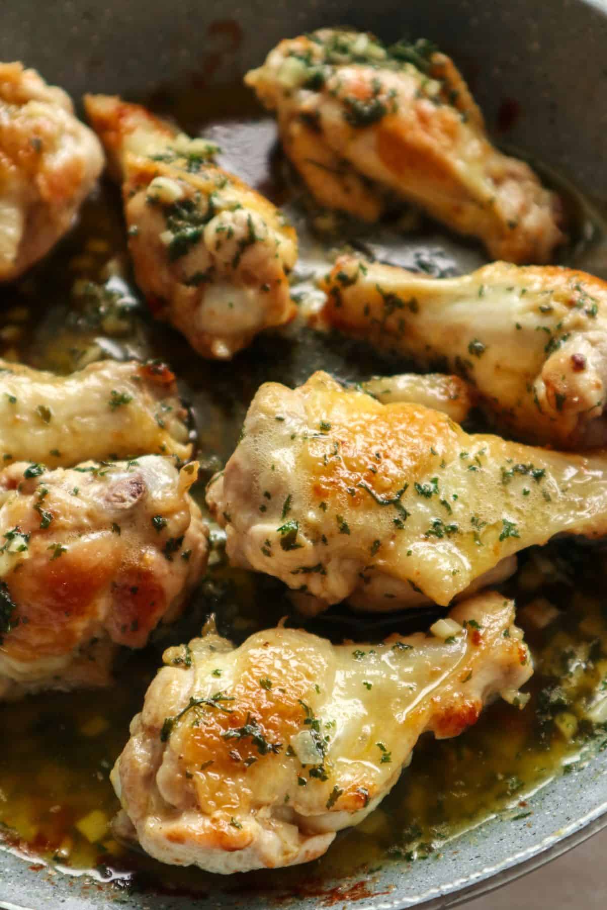 perfectly cookes garlic butter wings in a blue pan with fresh parsley