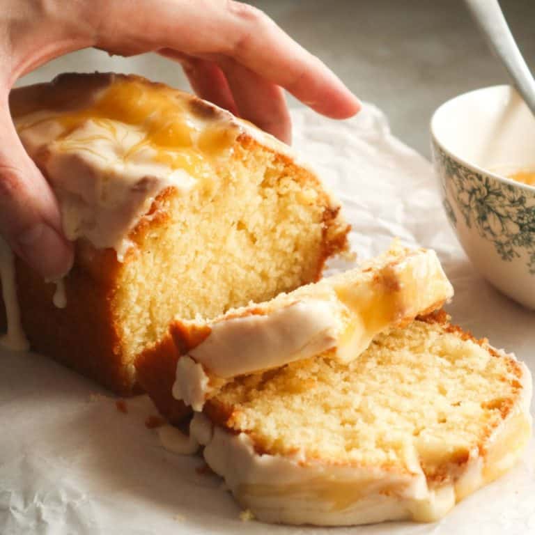 Featured image for my lemon curd cake recipe with a cake beeing picked up by a hand.